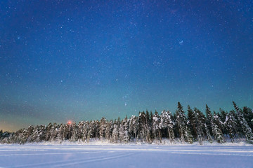 Night sky with lots of stars over a snowy landscape with a forest and a frozen lake, Sweden, Lapland