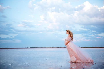 Fototapeta na wymiar beautiful young pregnant woman enjoying the sun on the beach, pink lake