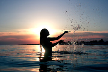 Fototapeta na wymiar girl silhouette at sunset sea splashing water hands summer