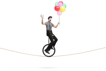 Mime riding a unicycle on a rope, holding a bunch of colorful balloons and waving © Ljupco Smokovski