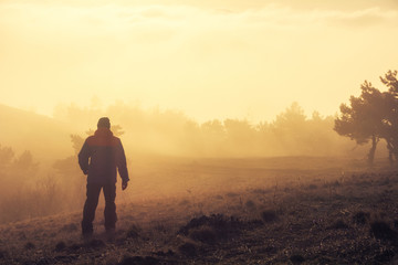 Alushta, Republic of Crimea - March 1, 2019: Alone tourist goes through the mist sunset sunlight across the mountain Demerdzhi