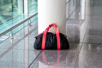 Suspicious black and red bag left unattended in an empty hall. Concept of terrorism and public safety. Dangerous ownerless derelict luggage. - obrazy, fototapety, plakaty