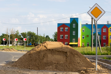 sidewalk repair along the highway. a pile of sand for the substrate for paving slabs. The colorful house in the background is a kindergarten