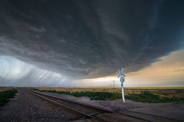 A large storm blows in over a railroad crossing, dumping heavy rain and producing extreme winds.