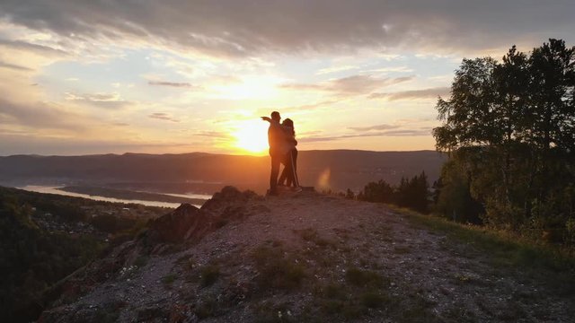Silhouettes of a pair of young men kissing on top of a mountain at sunset.