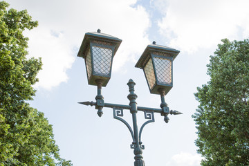 Ancient street lamp on the background of trees clouds of blue sky. The architecture details of the design.