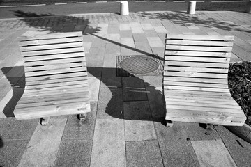 A pair of wooden benches on the sidewalk with long ones in black and white. Architecture style.