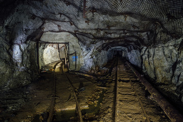 Dark dirty abandoned uranium mine with rusty remnants of railway