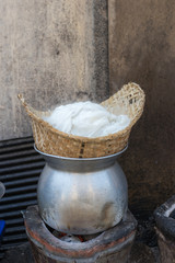 sticky rice is streaming in bamboo basket steamer on stainless pot with charcoal