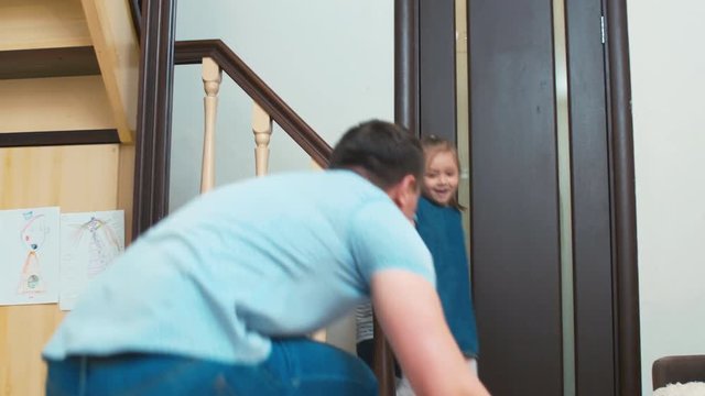 Little sister and brother going down stairs at home, while father bringing box with puppy to them, and jumping with happiness after finding out the present