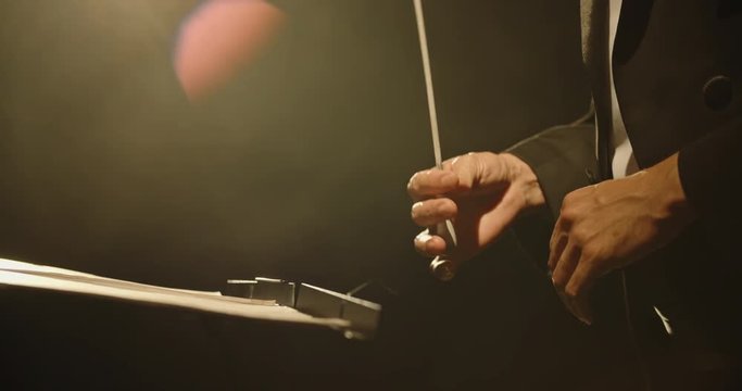 Close up shot of hands of symphony orchesra conductor directing music by waving his baton. Studio shot on black background 4k footage