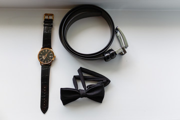Composition of men's accessories. Expensive wrist watch, black classic butterfly, black leather strap top view.