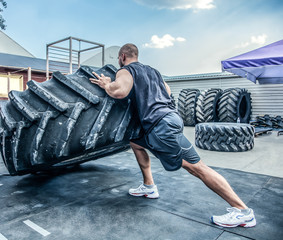 back view of strong muscular fitness man moving large tire in street gym. Concept lifting, workout...