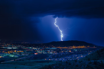 A vivid lightning bolt striking the ground behind a hill at night - Powered by Adobe