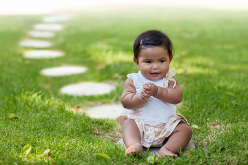 A baby girl grasping her own hands while sitting on the frontmost stepping stone from a series of stepping stones that go into perspective.
