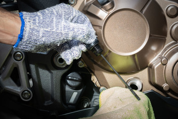 Hand of technician wearing cloth gloves check lubricant engine oil level motorcycle bigbike. maintenance motorcycle concept in garage or check before you travel.