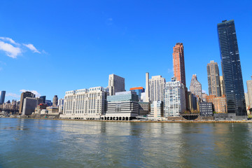 Manhattan skyline in the morning as seen from Roosevelt Island in New York, USA. Urban landscape with river view and bright blue skies.