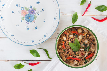 Thai food name Pad Ka Prao,Top view image of Stir-fried pork with basil leaves beside have flower pattern dish on white wood table background