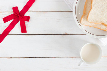 Top view image of Sliced bread on dish with hot milk in white cup and Corner have ribbon on white wood table background, Breakfast in morning, Fresh Homemade, copy space