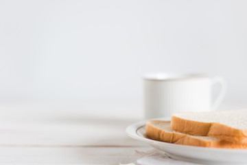 Select focus Sliced bread on dish with hot milk in white cup on white wood table background,...