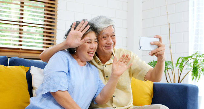 Senior Asian Couple Make Video Call To Family, Friend Smiling With Happiness While Sitting At Sofa In Home Living Room, Old People And Technology Lifestyle, Active Senior Retirement