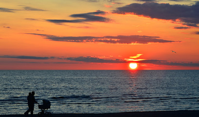 Fototapeta premium Silhouettes of walking people on sandy beach of the Baltic Sea during colorful sunset