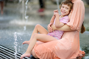 Portrait of beautiful disabled girl in the arms of his mother having fun in fountain of public park...