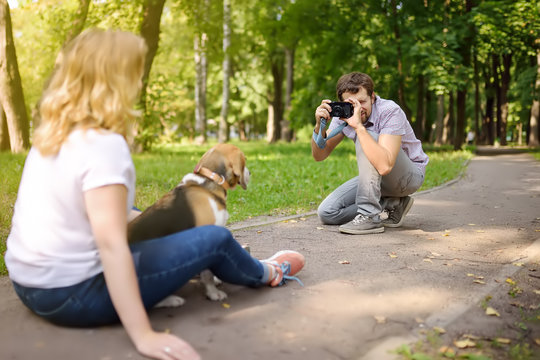 Young man take a shot beautiful woman with dog in sunny summer park. Date or walking.