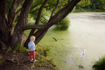 Upset or offended little boy standing on the shore of the pond. Child lose yourself. Kid run away. Escape from the house.