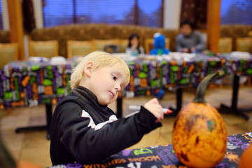 Little boy in scary skeleton costume paints pumpkin on halloween party for children.