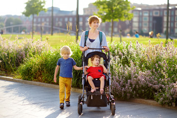 Woman with a boy and a disabled girl in a wheelchair walking in the park at summer. Child cerebral...