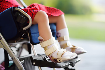 Disabled girl sitting in wheelchair. On her legs orthosis. Child cerebral palsy. Inclusion.