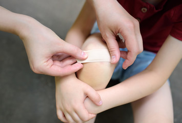 Mother hands applying antibacterial medical adhesive plaster on child's knee after falling down.