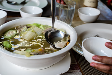 Woman's hand and scooping slice of Pompano fish soup into a small bowl. Pompano fish or Jack also known as Pampano for Filipinos or Trachinotus blochii.