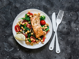 Warm chickpeas, cherry tomatoes, spinach salad and baked salmon - healthy lunch on a dark background, top view