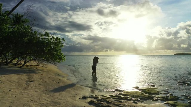 Young female photographer girl taking photos on beach against sunset sunrise tropical island in the Maldives