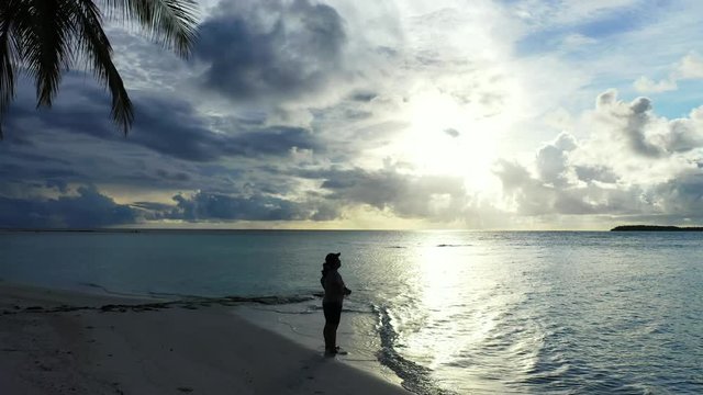 Young girl with a camera taking pictures on the beach at sunset in the Maldives Islands, Indian Ocean