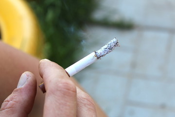 Male hand holding a smoldering cigarette in the street