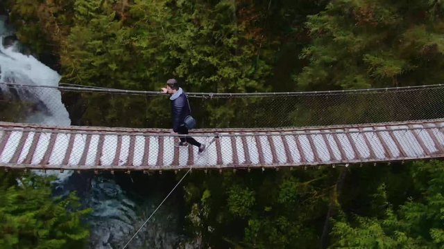 Man walking on suspension bridge, drone shot of man on suspension bridge. Capilano and Lynn valley canyon.