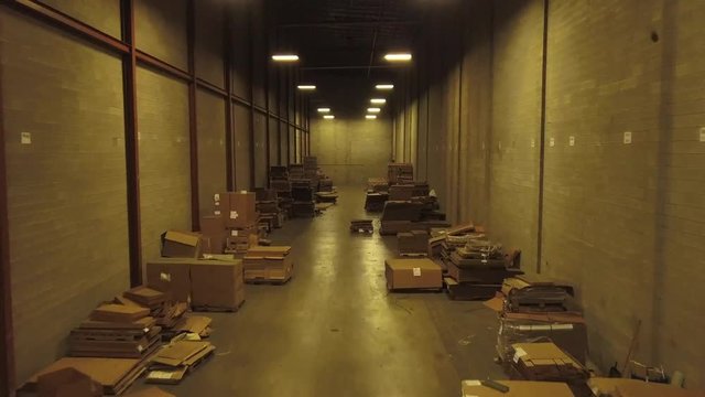Aerial footage of boxes and files stacked on floor of a warehouse. Drone moves slowly forward between two wooden walls lined by piles of stuff on the floor.