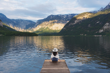 Young woman sitting alone on wooden pier, looking lake and mountain view in summer at Hallstatt, Austria