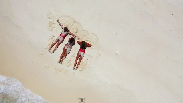 sexy young women sunbathing and making shapes in the sand on tropical beach,