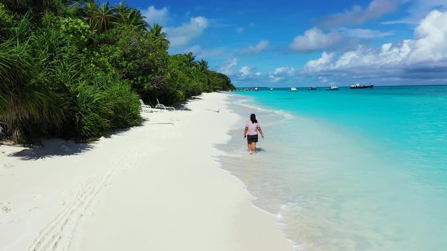 A woman walking along the beach in the middle of the frame. The turquoise Caribbean Sea. Wide angle, dolly in