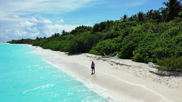 A woman is walking along the beach through of turquoise blue water. In the Caribbean.
