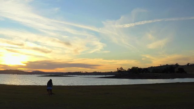 Aerial, drone shot panning around a woman, walking on a beach, at lake Huma, at sunset,, on a sunny evening, at Hume Reservoir, between New South Wales and Victoria, in Australia