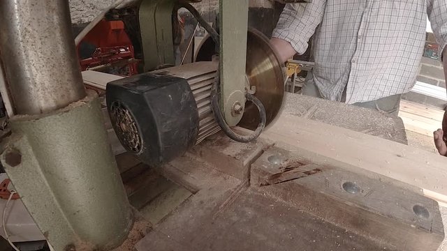 Cutting a wooden board lengthways with a bench mounted circular saw.