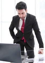 Businessman standing at his Desk and looking at the laptop screen