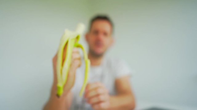 Man in defocussed background peels and eats foreground bananna. Locked off