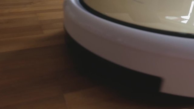 Cloes Up shot of a white suction cleaner robot drives towards the camera, stops and turns whilst cleaning a laminate floor
