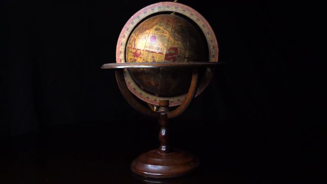 This zooming out video shows a spinning antique medieval old world globe with a black background.